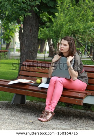Young student woman hugging her laptop while sitting on a bench in a park.