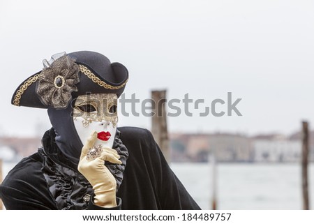 VENICE-MARCH 2:Portrait of a disguised person with a white mask and black costume thinking on a pier on March 2 2014 in Venice,Italy.