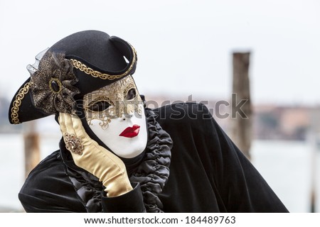VENICE-MARCH 2:Portrait of a disguised person with a white mask and black costume thinking on a pier on March 2 2014 in Venice,Italy.