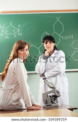 Girls in lab coats with microscope and chemical formula on background