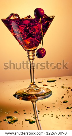Martini glass with ice cubes and red drink with cherries