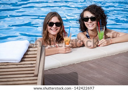 Two attractive young women enjoying swimmer pool and cocktails