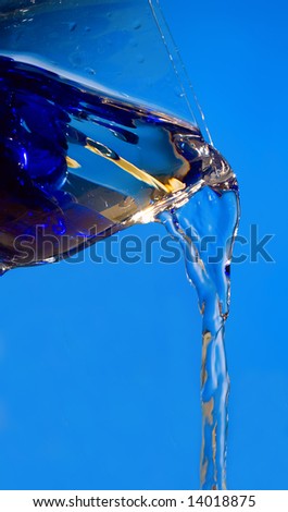 Pure liquid pouring from glass over blue background