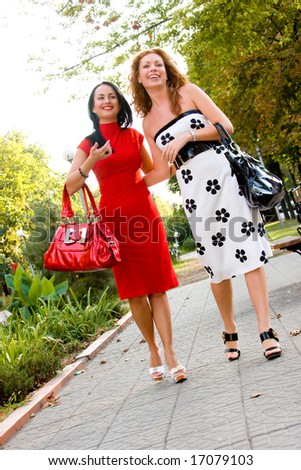 Two young pretty women walking with bags across park