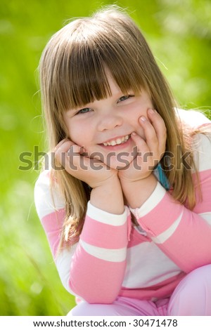 Pretty little girl wearing pink blouse on green summer grass background