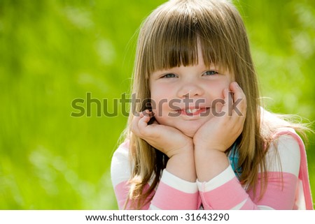Pretty little girl wearing pink blouse on green summer grass