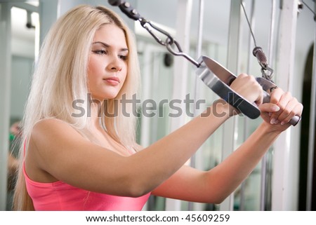 Pretty blond woman exercising on pulldown station in gym