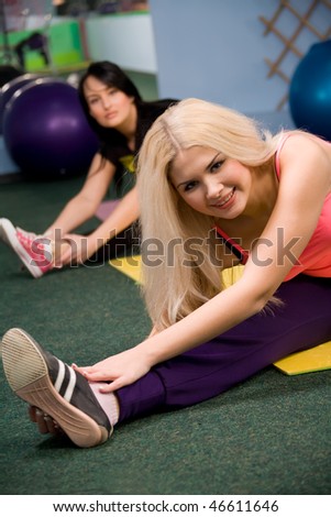 Young women, blond and brunette stretching on gym floor