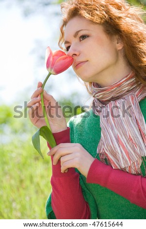 Beautiful young red-haired woman smelling red tulip on green meadow