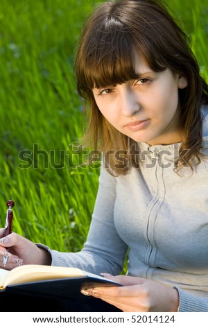 Pretty college girl studying a book on green meadow