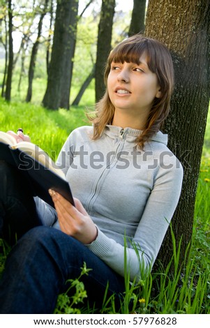 Pretty college girl studying a book on green meadow