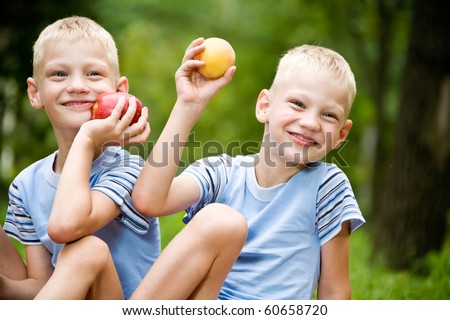Two smiling twin brothers holding fruits outdoor portrait