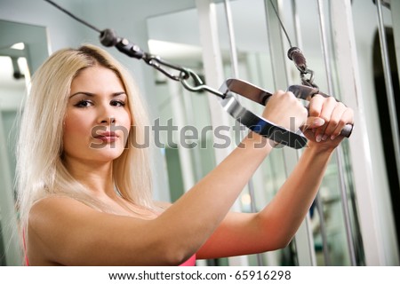 Pretty blond woman exercising on pulldown station in gym
