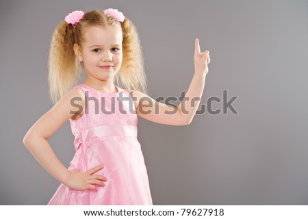 Cute little girl in pink dress pointing with finger toward empty space