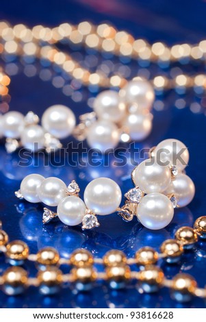 Pearl earring and golden beads on blue background