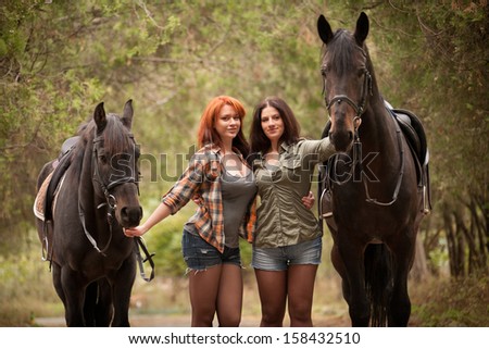 Young women walking with horses along forest lane