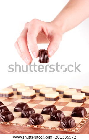 Hand holding chocolate candy over chess board with candies arranged as chess
