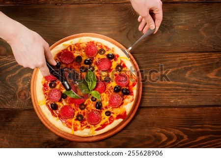 Hands cutting pizza on wooden table from top view