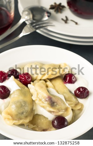 Cherry dumplings with sour cherry and cream on a white plate and cherry juice