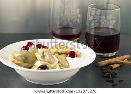 Cherry dumplings with sour cherry and cream on a white plate and cherry juice