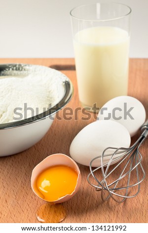 Baking ingredients. Milk, flour, eggs, whisk on the wooden board