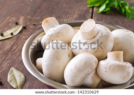 Bunch of fresh white mushrooms in the purple bowl on a wooden background