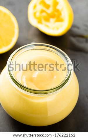 Homemade lemon curd in glass jar on fresh lemon background