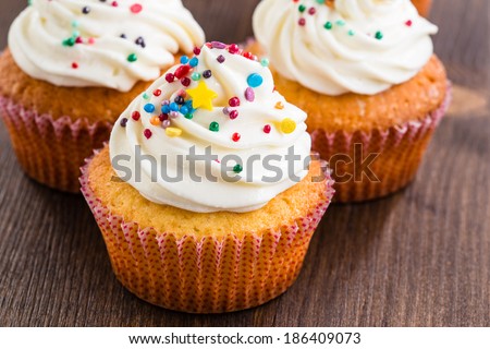 Gourmet cupcakes with white buttercream frosting and sprinkles on wooden background