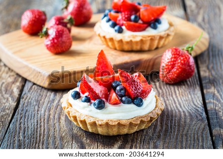 Fruit dessert tarts with cream, strawberry and blueberry on wooden table