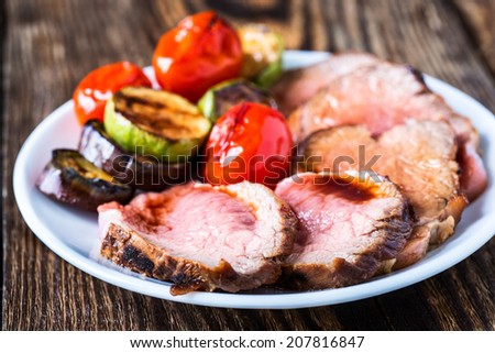 Sliced rare roast sirloin of beef with roasted vegetables on rustic wooden background