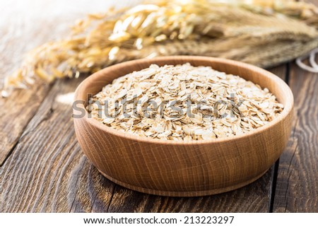 Rolled oat flakes in a wooden bowl and oat stalks