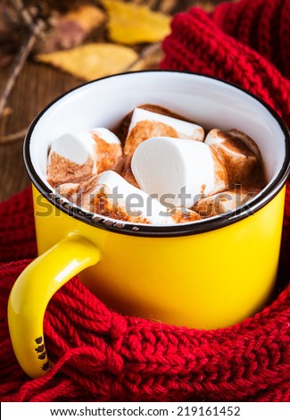 Mug full of hot chocolate with marshmallow on a knitted woolen scarf. Warming drink for fall and winter
