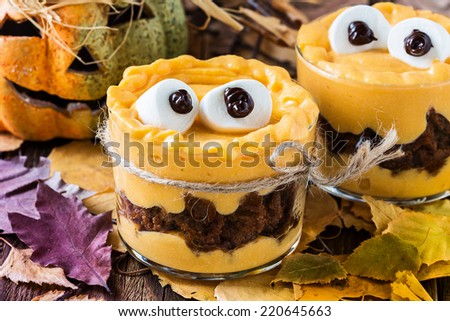 Halloween treats, little monster dessert with chocolate cookies and orange pumpkin  mascarpone cream  topped with big marshmallow eyes