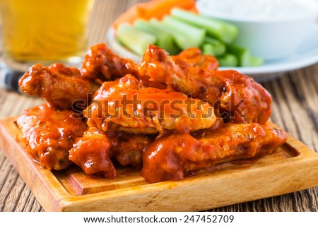 Buffalo chicken wings with cayenne pepper  sauce served hot with celery sticks and carrot sticks with blue cheese dressing for dipping and beer
