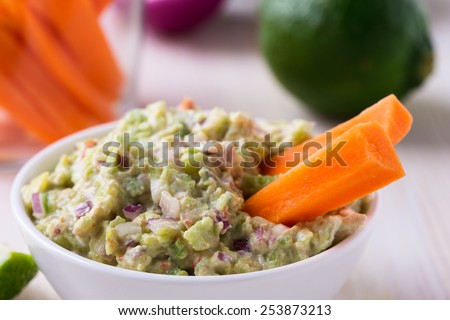Healthy homemade guacamole, dip with  avocado, lime juice,  tomato, onion, and cream cheese served  with carrot sticks