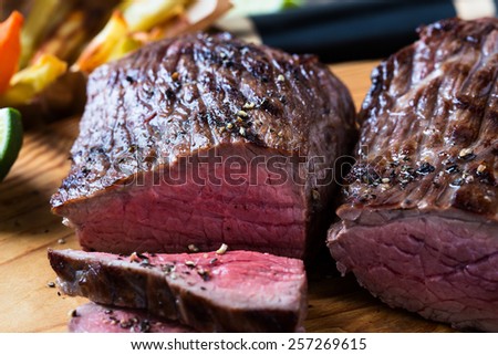 Rare roast beef sirloin with french fries and slices baked pumpkin chips on cutting board