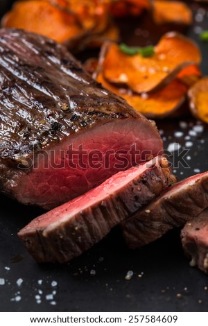 Rare roast beef sirloin with slices baked pumpkin chips on gray board