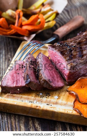 Rare roast beef sirloin with french fries and slices baked pumpkin chips on cutting board