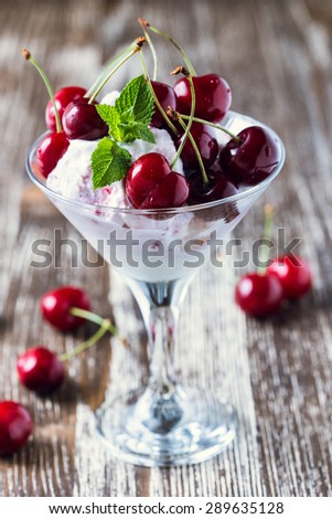 Frozen fruit soft ice cream dessert with sweet cherry on top in martini glass on shabby chic background