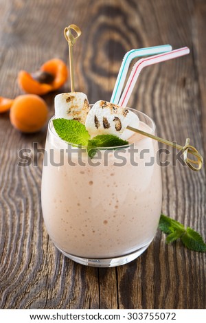 Homemade fresh summer fruits milkshake with toasted marshmallow and ripe apricots on rustic wooden background