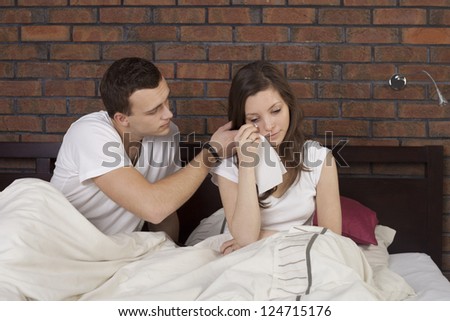 A young man consoling crying woman in the bed