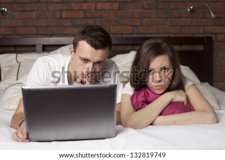 Young man using laptop in the bed and angry woman