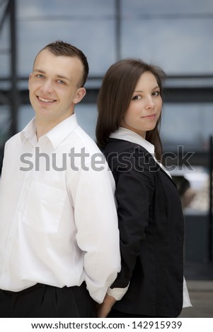 Woman and man in suit standing in front of a building. Background is out of focus.