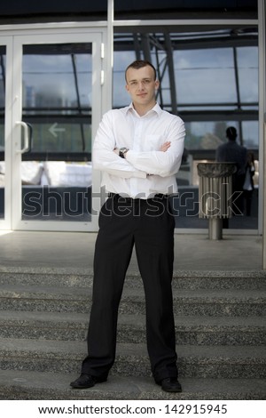 Man in suit standing in front of a building. Background is out of focus.