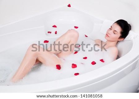 beautiful young woman relaxing in bubble bath with rose petals