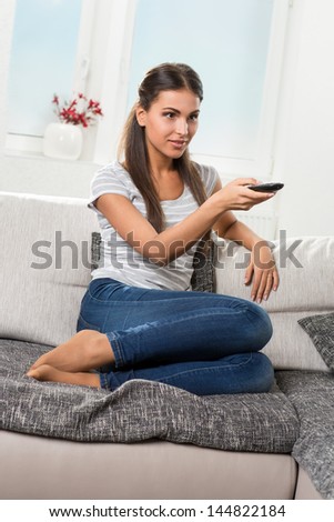 woman sits at a loss on the couch with remote control, watching TV