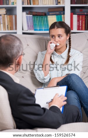 Teenage girl crying on sofa during therapy session while therapist is taking notes