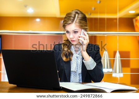 Young girl sitting in a cafe with a laptop and talking on cell phone