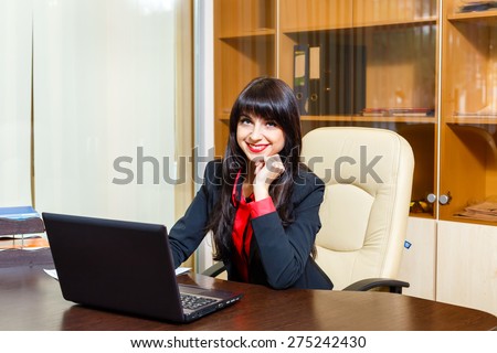 Smiling nice businesswomen sitting at the table in the office with paperwork and laptop