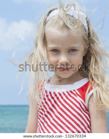 Cheerful girl with disheveled hair in the wind at the beach on a sunny day, close-up  against the sky and the sea